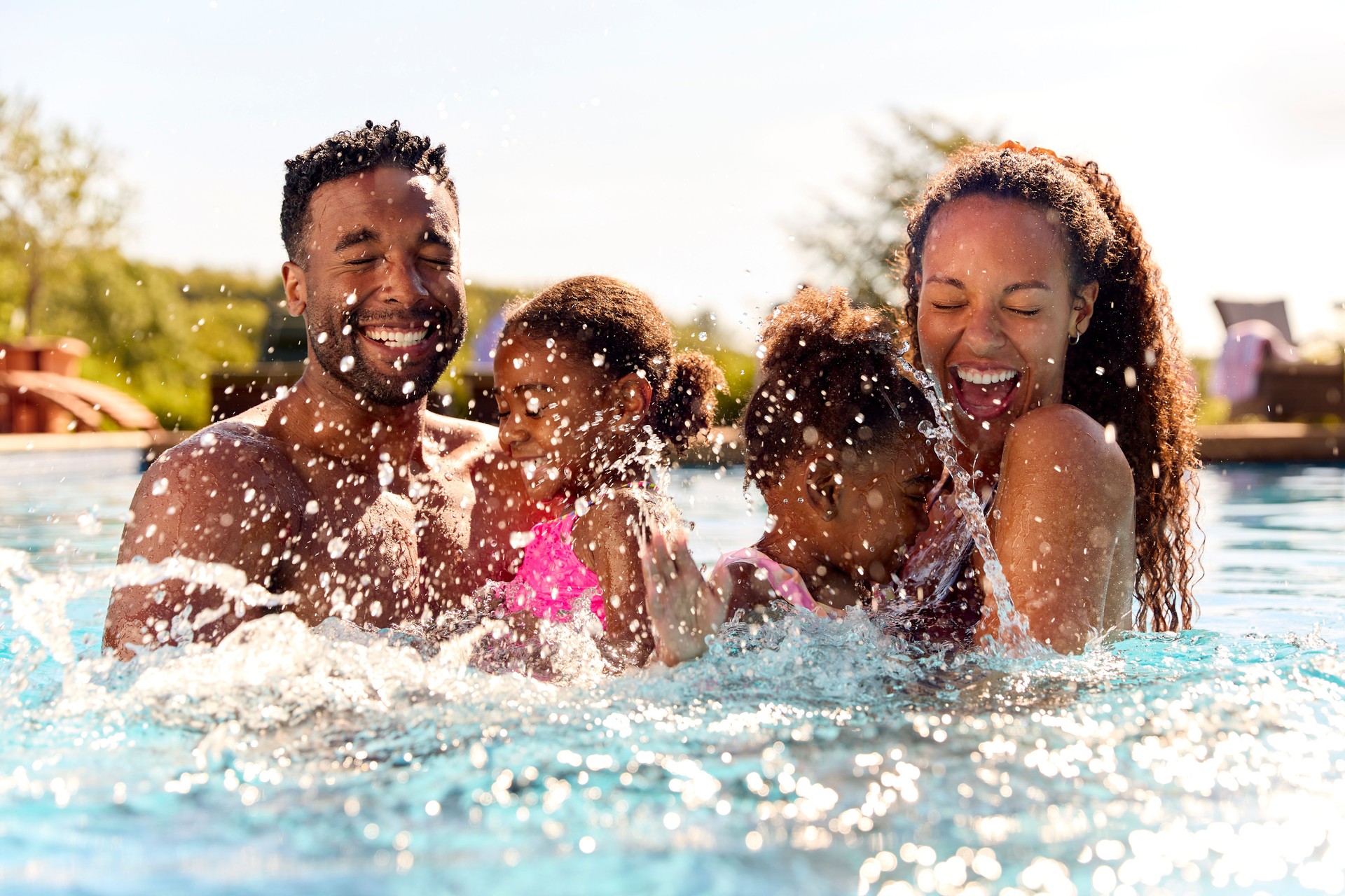 Family On Summer Holiday With Two Girls Being Held In Swimming Pool By Parents And Splashing